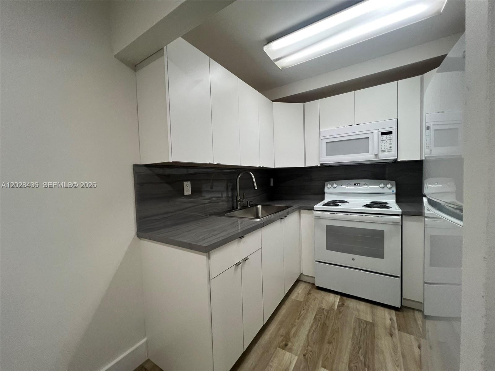 A kitchen features white cabinets, a dark gray countertop, and white appliances — 5644 W 25th Ct # 5644, Hialeah FL 33016, HIALEAH, FL