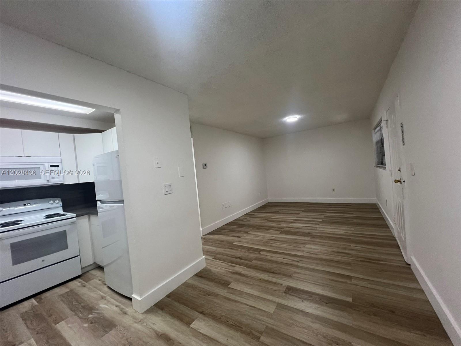 An open-plan living area features wood-look flooring and a view into a white kitchen — 5644 W 25th Ct # 5644, Hialeah FL 33016, HIALEAH, FL