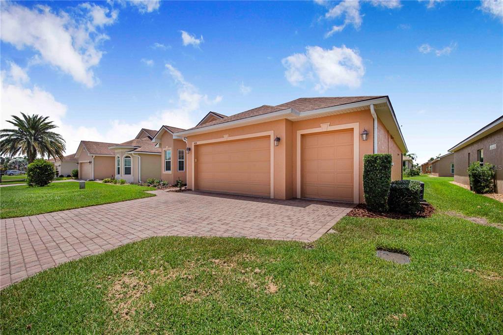 A tan house with a three-car garage and a paved driveway under a blue sky — 4084 STONE CREEK LOOP, LAKE WALES, FL