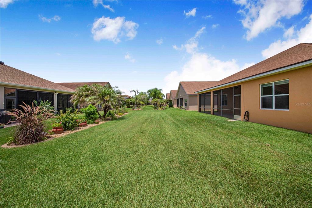 A grassy backyard area sits between two houses with screened-in lanais under a blue sky — 4084 STONE CREEK LOOP, LAKE WALES, FL