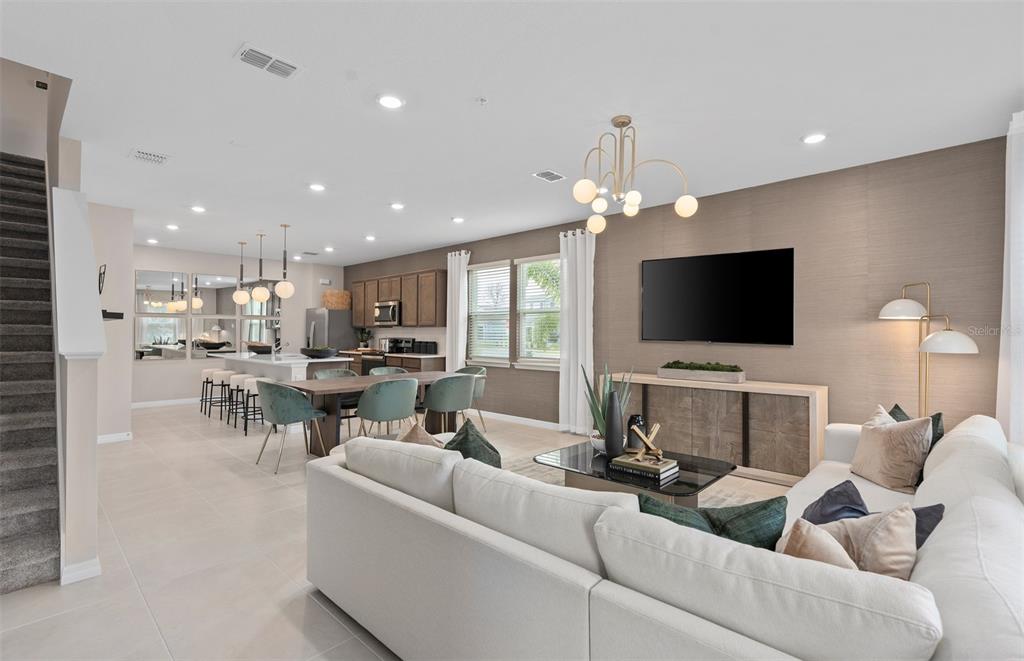 A modern open-concept living room and kitchen featuring a white sectional, dining area, and cabinetry — 11365 NONA SOUND STREET, ORLANDO, FL