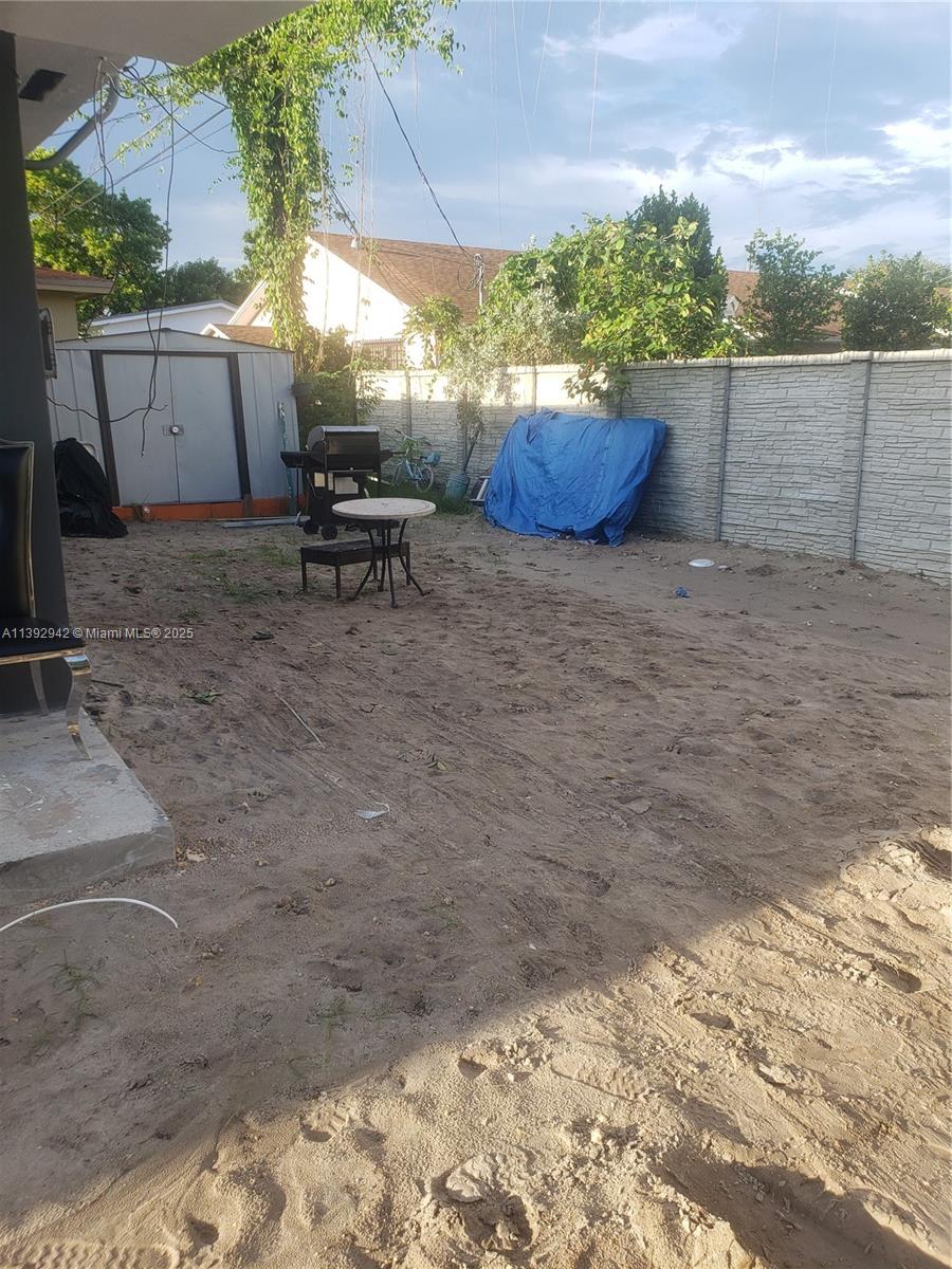 A sandy backyard features a metal storage shed, a small table, and a concrete fence — 2865 NW 22nd Ave, Miami FL 33142, MIAMI, FL