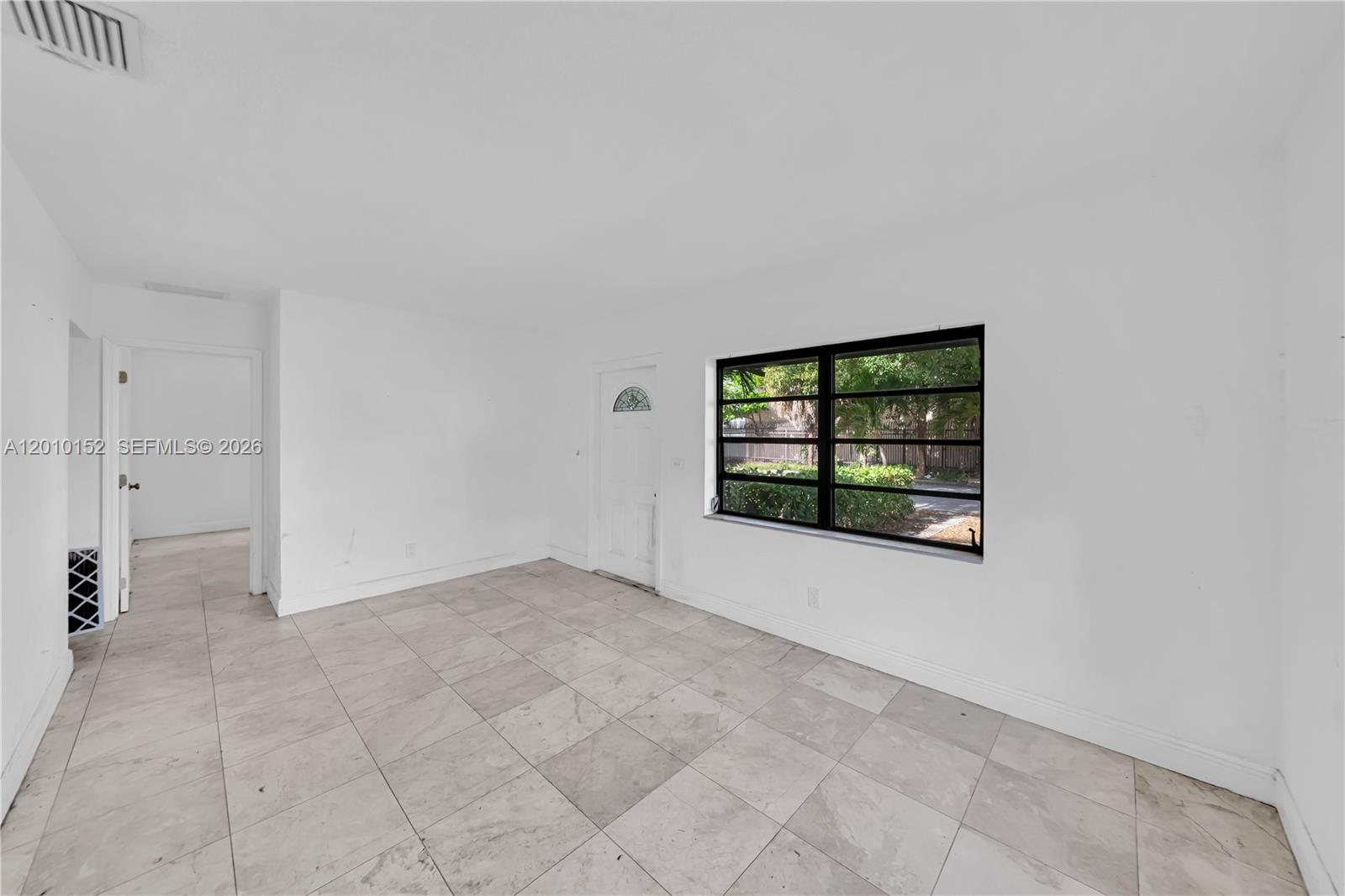 An empty room features white walls, light-colored tile flooring, a window, and a white door — 3033 Hibiscus Street, Miami FL 33133, MIAMI, FL