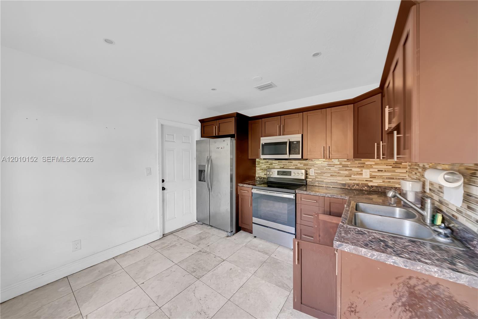A kitchen features brown cabinets, stainless steel appliances, a tiled backsplash, and light floor tiles — 3033 Hibiscus Street, Miami FL 33133, MIAMI, FL