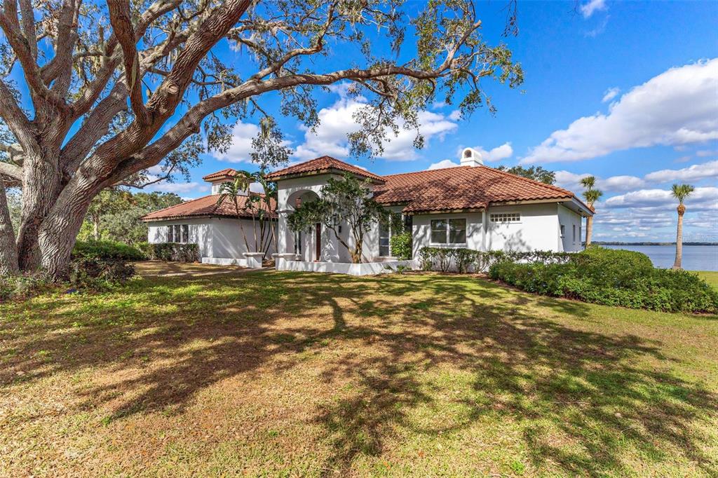 A white, single-story house with a red tile roof sits on a grassy waterfront lot — 38230 YALE CIRCLE, LEESBURG, FL
