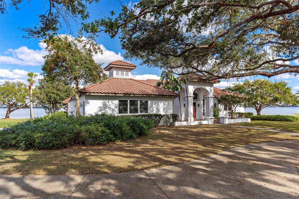 A white house with a red tile roof sits on a grassy lot near water — 38230 YALE CIRCLE, LEESBURG, FL