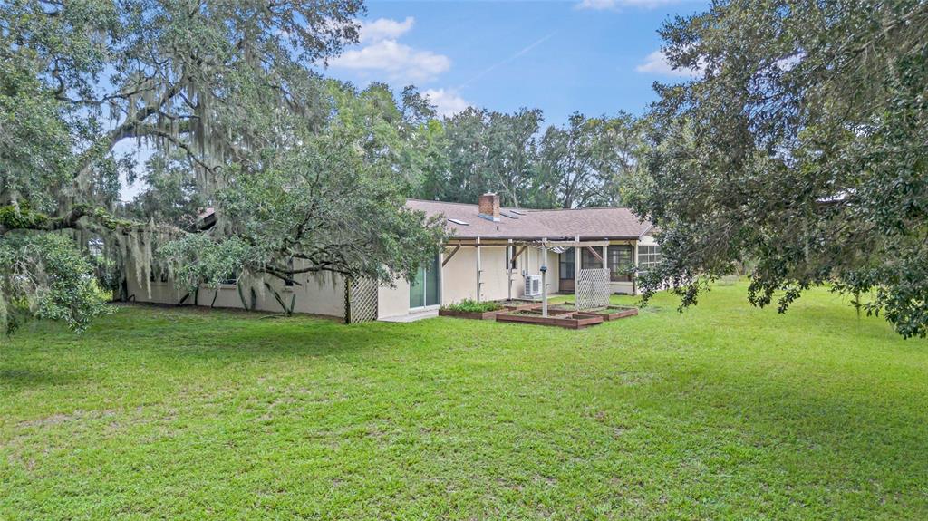 The exterior of a single-story house features a backyard with raised garden beds and trees — 53 N ARCHWOOD DRIVE, INVERNESS, FL