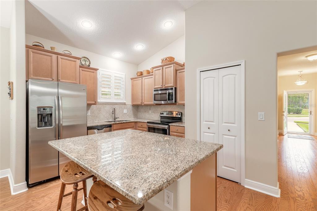 A kitchen features light wood cabinets, granite countertops, a center island, and stainless steel appliances — 3371 MEDICI BOULEVARD, NEW SMYRNA BEACH, FL