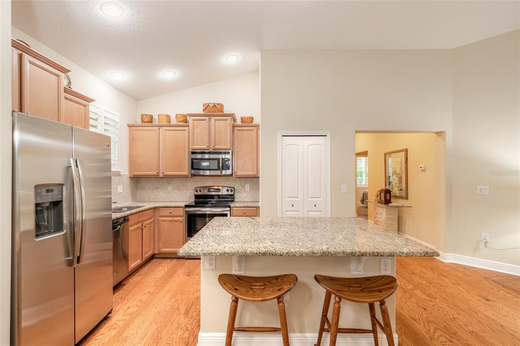 A kitchen features light wood cabinets, granite countertops, a center island, and stainless steel appliances — 3371 MEDICI BOULEVARD, NEW SMYRNA BEACH, FL