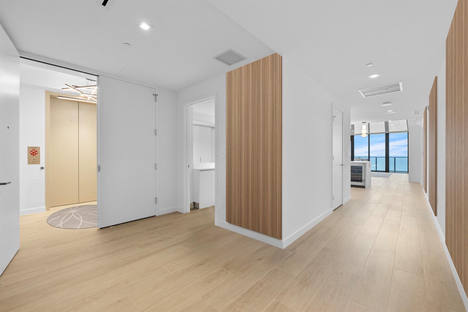 A modern hallway features light wood flooring, white walls, and vertical wood slat accent panels — 1116 N Ocean Boulevard # 904, Pompano Beach FL 33062, POMPANO BEACH, FL