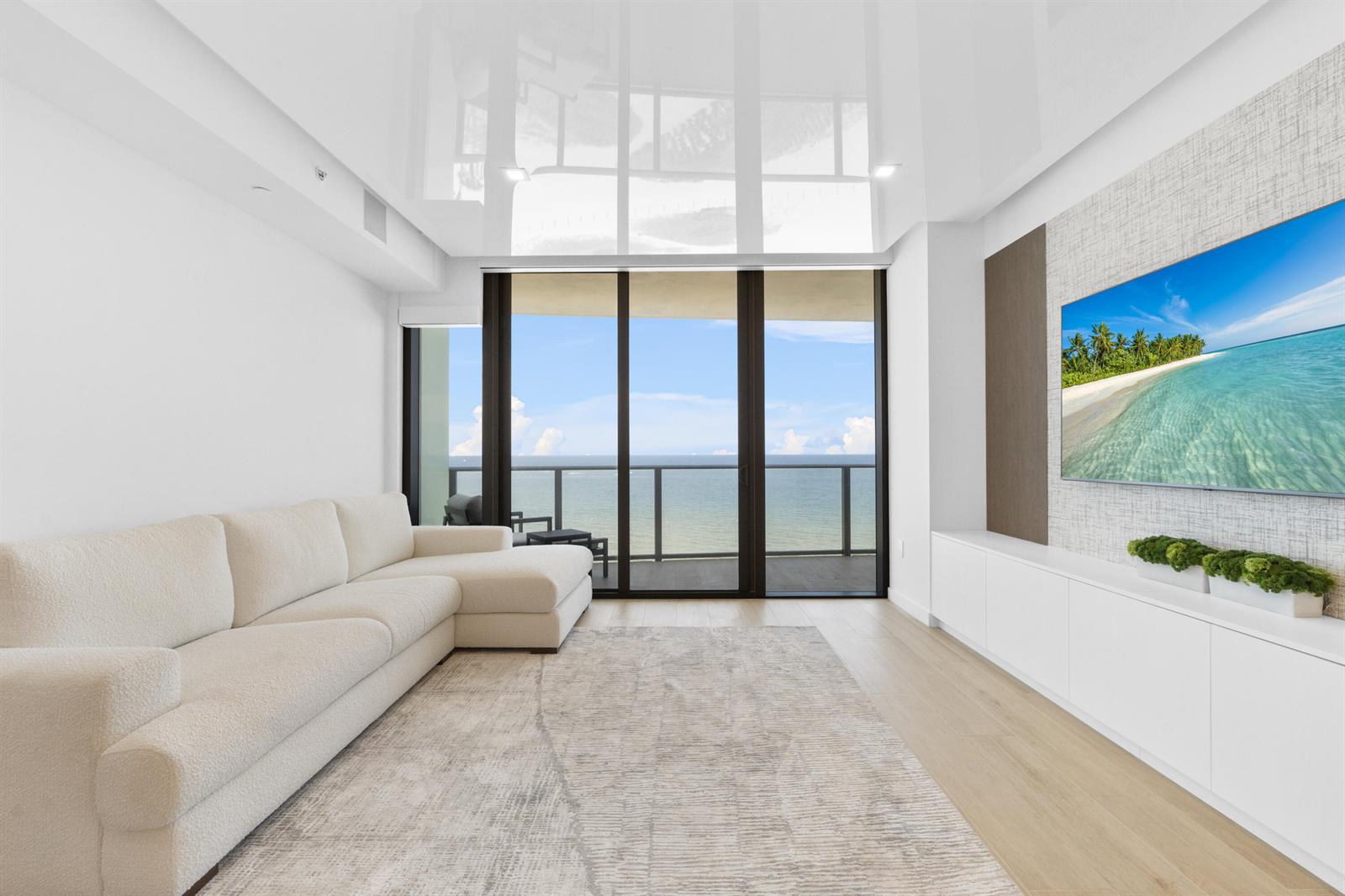 A modern living room features a white sectional sofa, media console, and floor-to-ceiling balcony windows — 1116 N Ocean Boulevard # 904, Pompano Beach FL 33062, POMPANO BEACH, FL