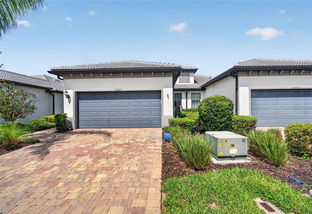 A single-story house exterior features a paver driveway, a gray garage door, and landscaping — 12287 MYRTLE BAY COURT, SARASOTA, FL