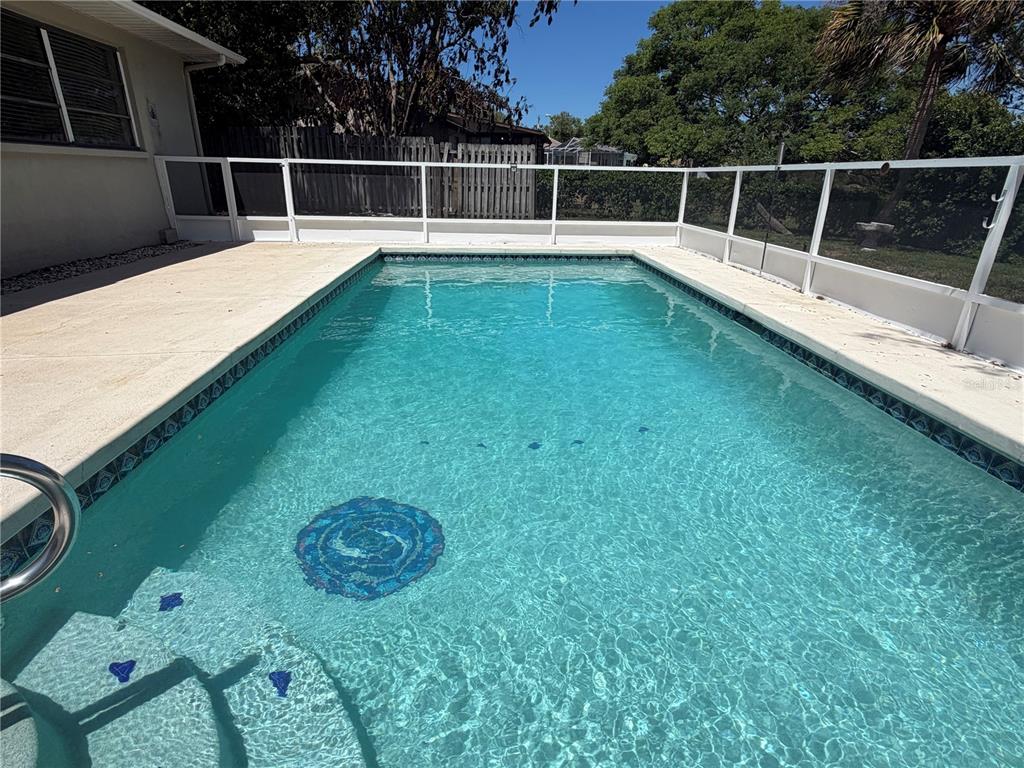 A rectangular swimming pool with a decorative mosaic tile inlay sits on a concrete patio — 1358 IVYDALE ROAD, SPRING HILL, FL
