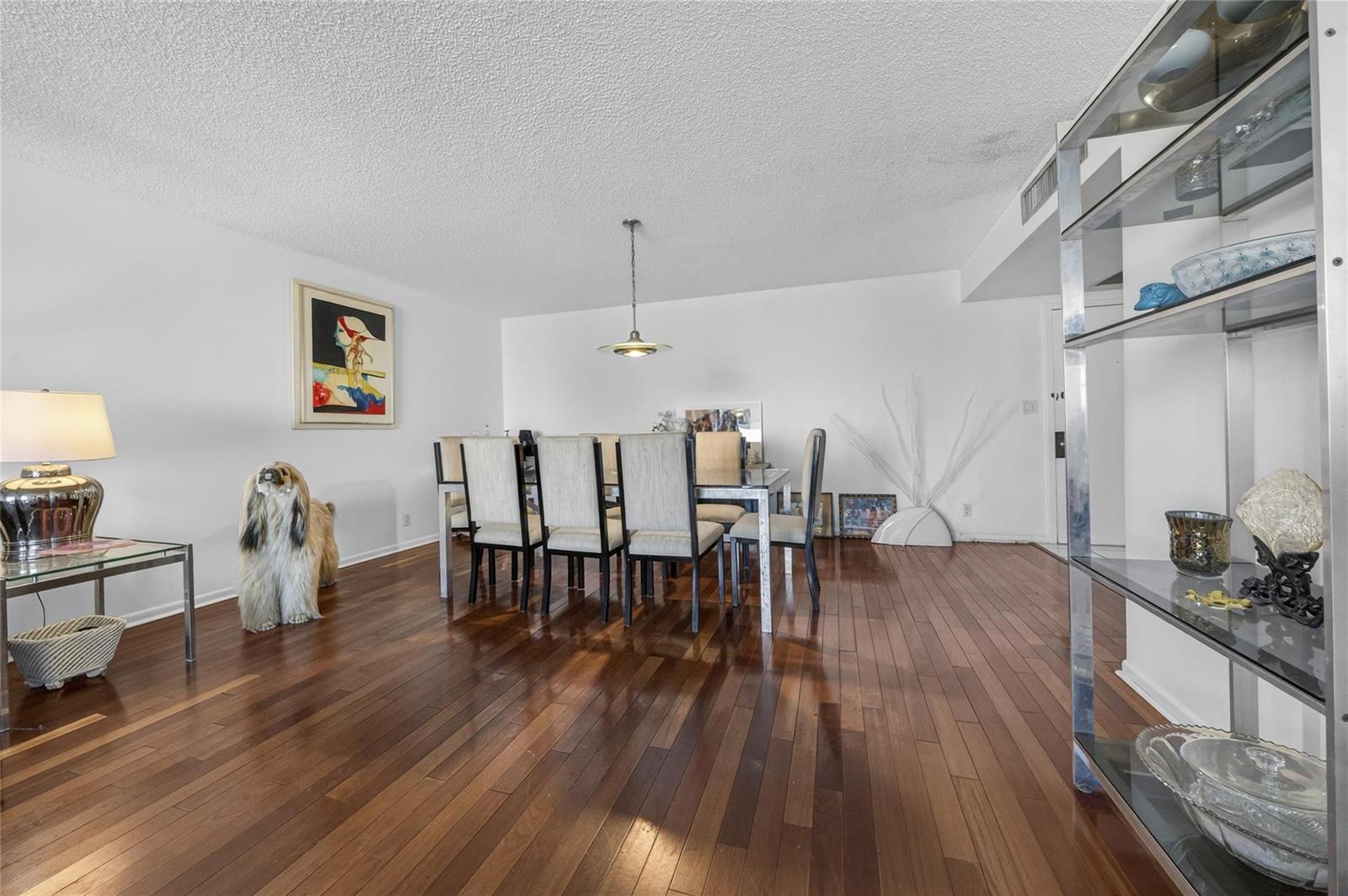 A dining room features dark hardwood floors, a glass-topped table, and a decorative dog statue — 600 Three Islands Boulevard # 406, Hallandale Beach FL 33009, HALLANDALE BEACH, FL