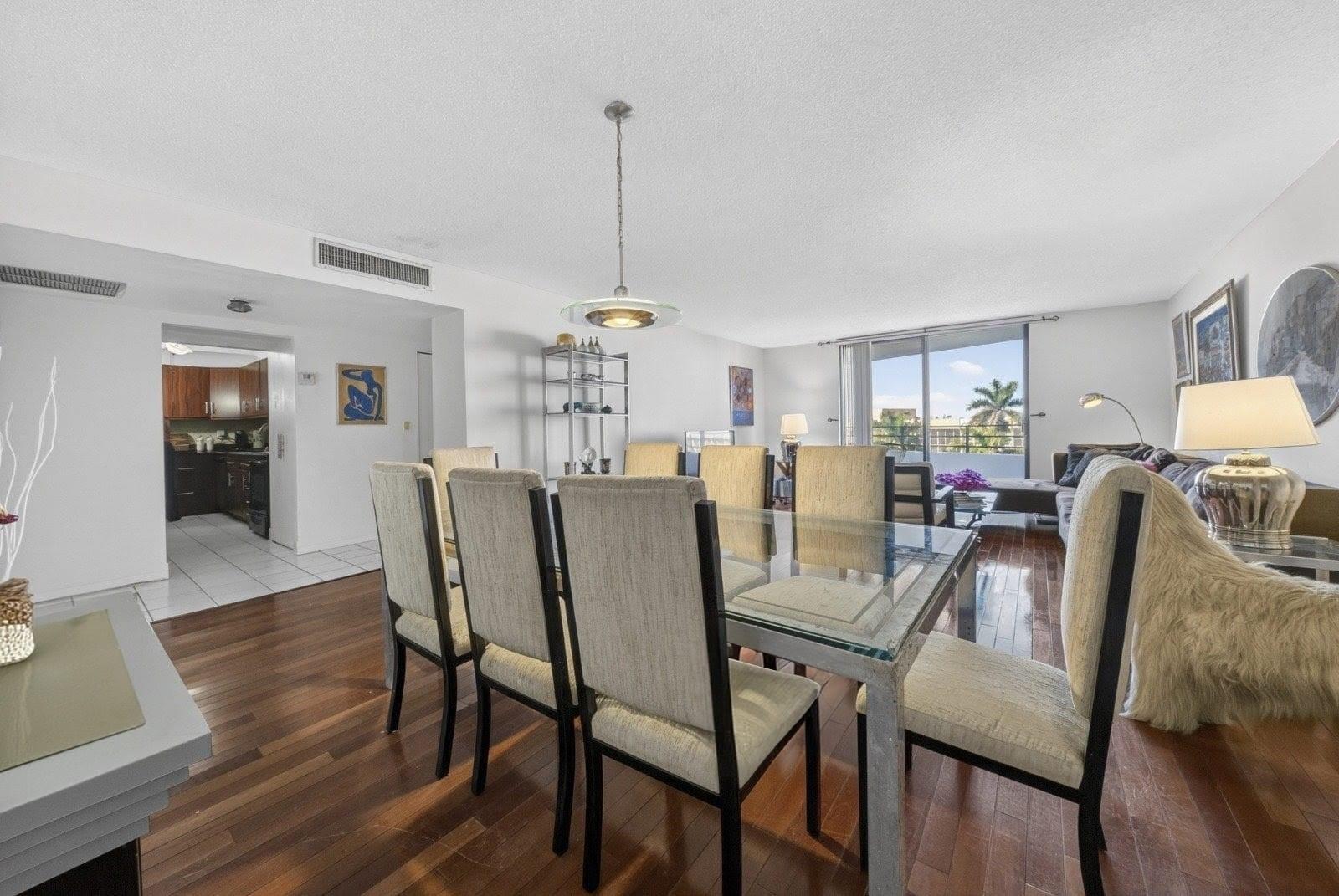 A dining area with a glass table and chairs opens into a living room and kitchen — 600 Three Islands Boulevard # 406, Hallandale Beach FL 33009, HALLANDALE BEACH, FL