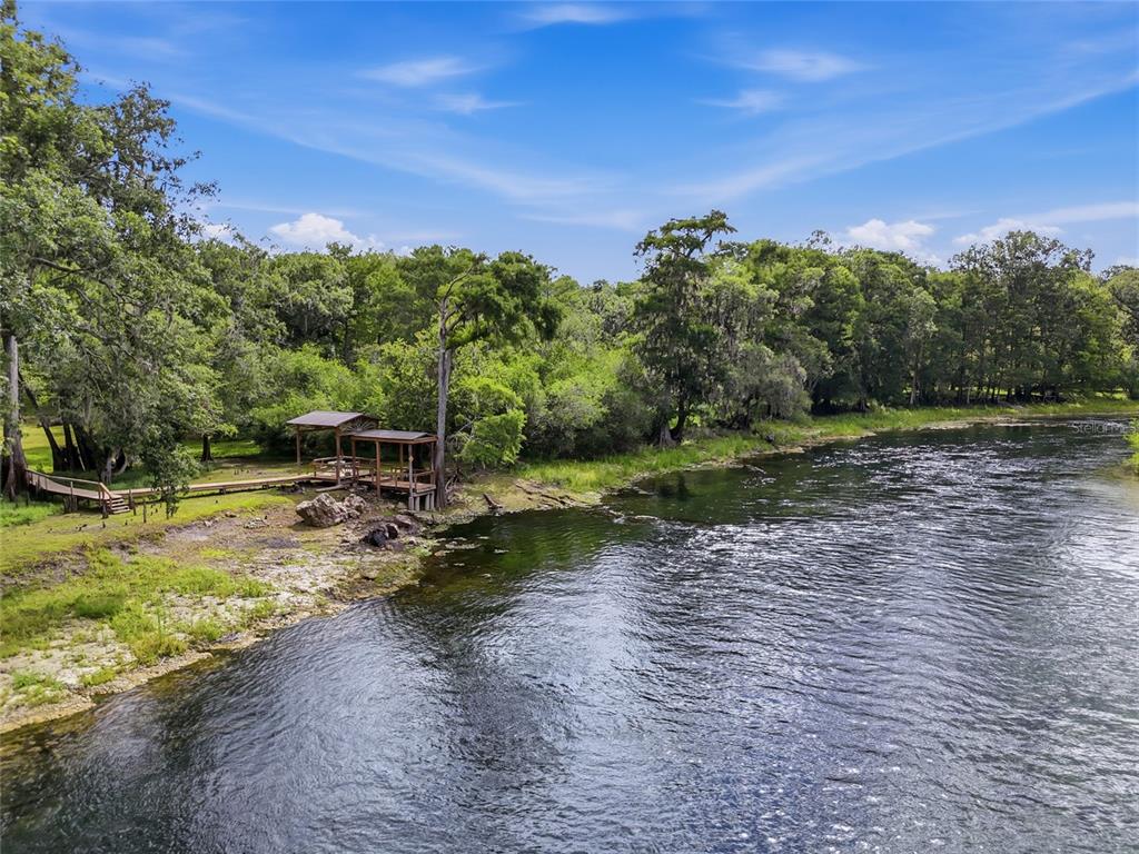 A wooden dock with a covered structure sits along a riverbank surrounded by trees — 470 SW SANTA FE DRIVE, FORT WHITE, FL