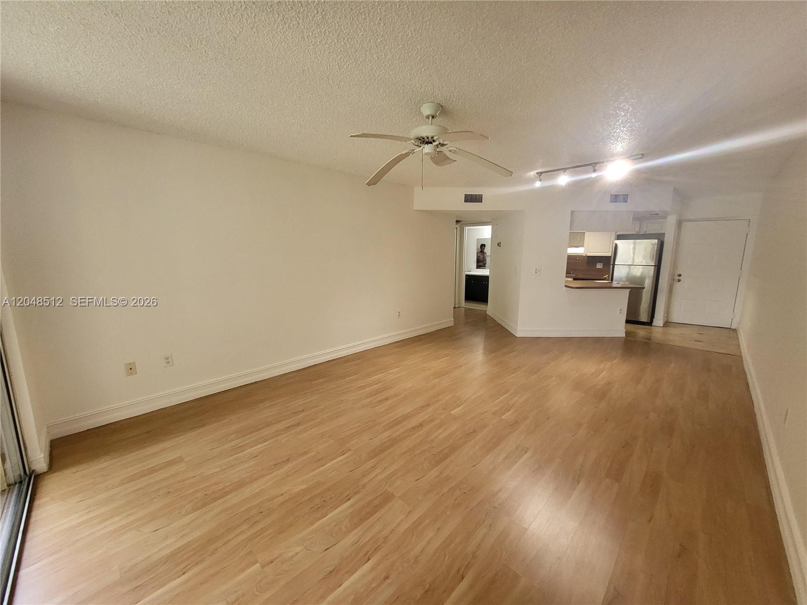 An empty living room features light wood-look flooring, a ceiling fan, and an adjacent kitchen — 8225 Lake Dr # 405, Doral FL 33166, DORAL, FL