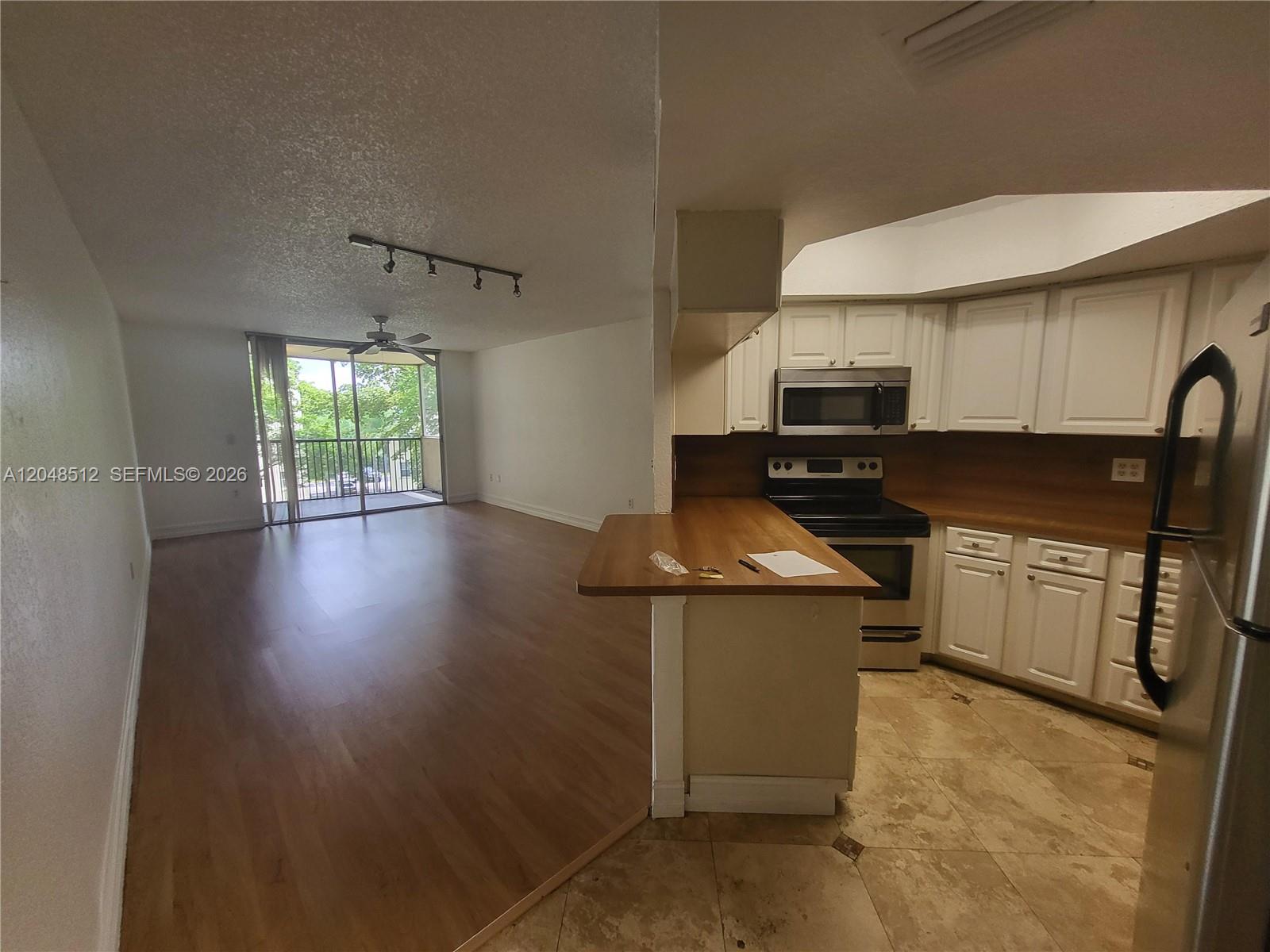 An open-concept kitchen with white cabinets and wood counters overlooks a living area with flooring — 8225 Lake Dr # 405, Doral FL 33166, DORAL, FL