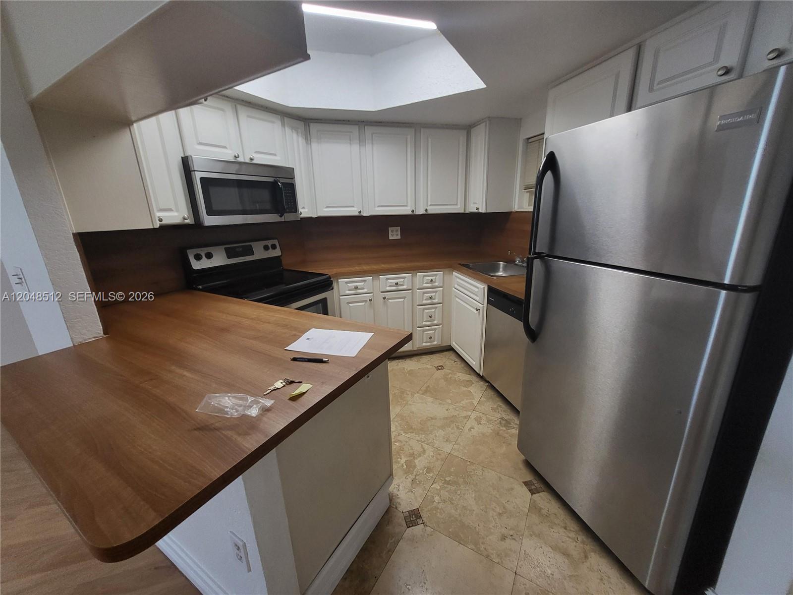 A kitchen features white cabinets, stainless steel appliances, wood countertops, and light-colored tile flooring — 8225 Lake Dr # 405, Doral FL 33166, DORAL, FL