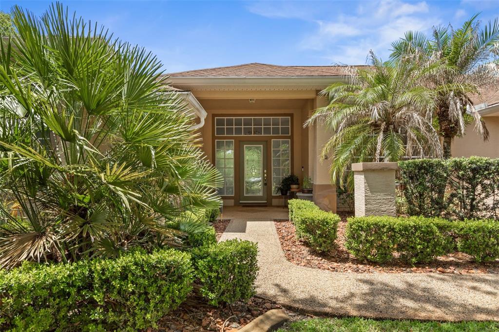 A front view of a house entrance with a walkway, palm trees, and manicured hedges — 22 IBIS COURT N, PALM COAST, FL