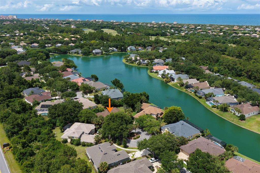 An aerial view shows a residential neighborhood with houses surrounding a lake near the ocean — 22 IBIS COURT N, PALM COAST, FL