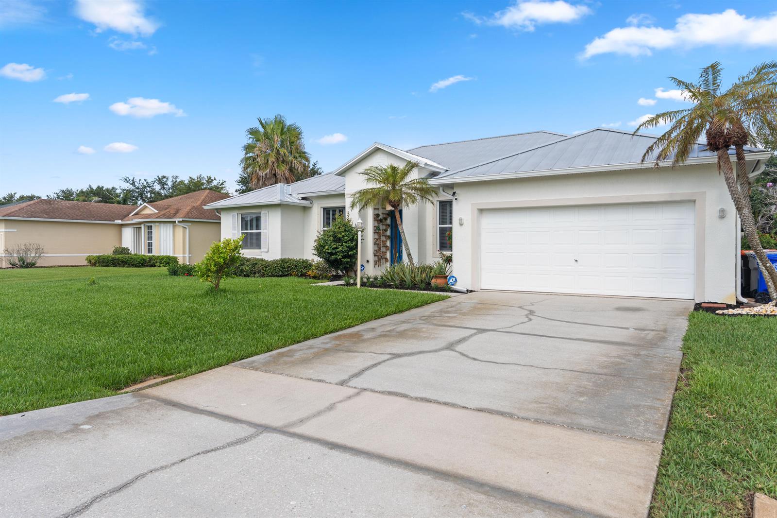 A single-story house with a white stucco exterior, metal roof, and a cracked concrete driveway — VERO BEACH, FL