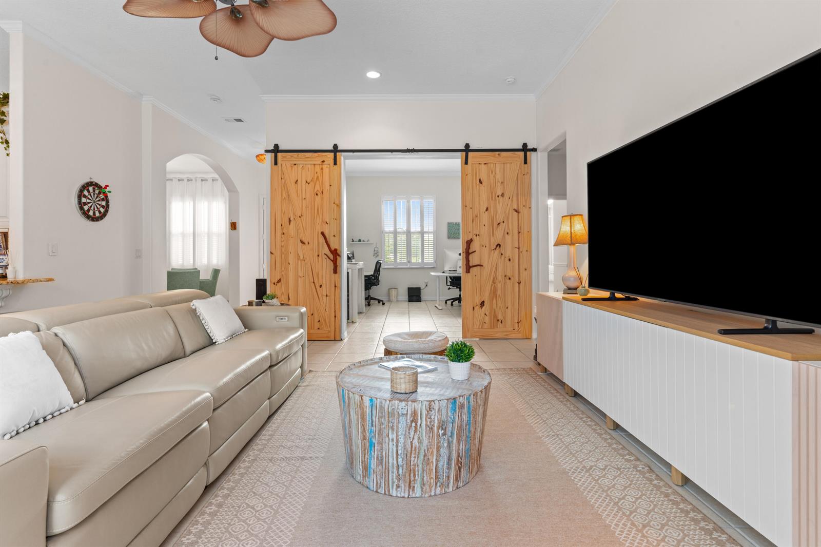 A living room features a beige leather sofa, a rustic coffee table, and wooden barn doors — VERO BEACH, FL