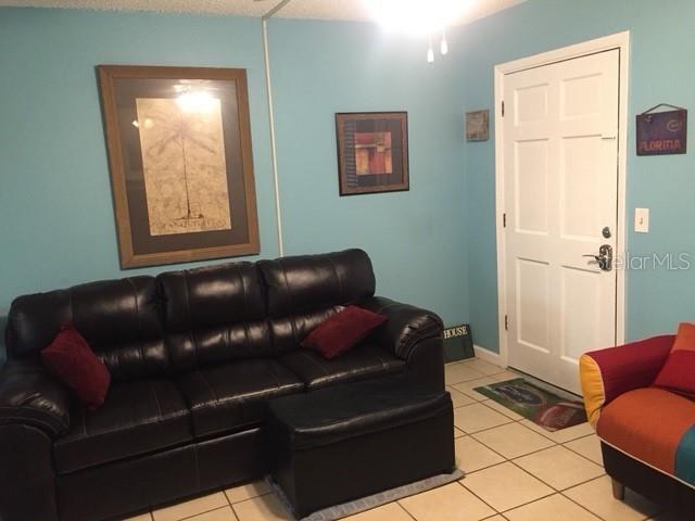 A living room features light blue walls, a black leather sofa, and a white door — 7710 BAYSHORE DRIVE UNIT 2, TREASURE ISLAND, FL