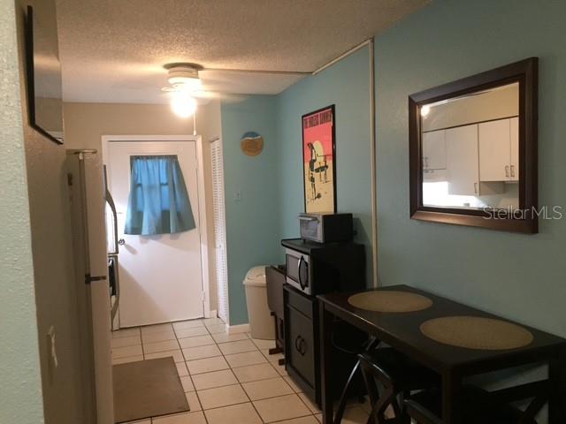 A kitchen area features a dining table, a microwave, and a door with a blue curtain — 7710 BAYSHORE DRIVE UNIT 2, TREASURE ISLAND, FL