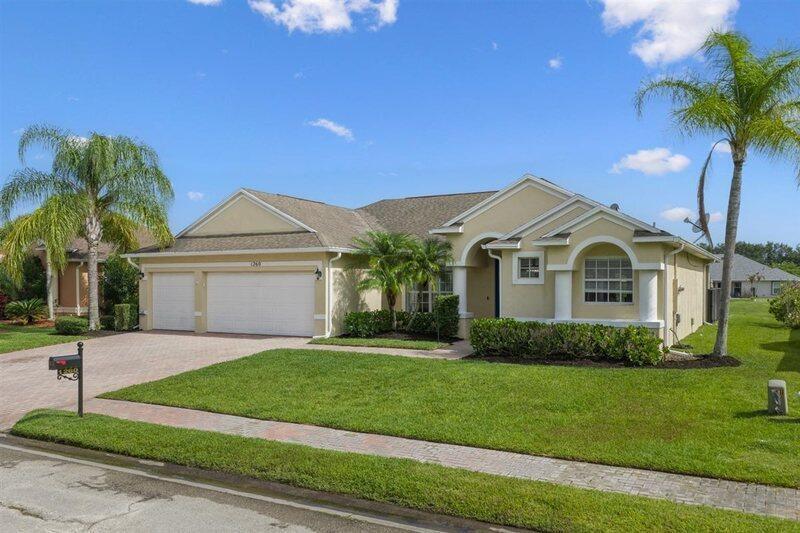 A single-story suburban house with a two-car garage, beige stucco exterior, and palm trees — VERO BEACH, FL