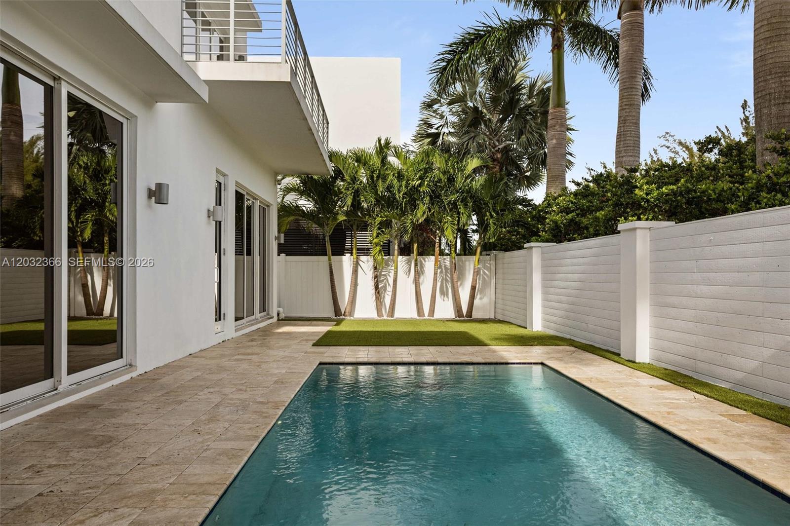 A rectangular swimming pool sits on a stone patio beside a modern white house — 10296 NW 74th Terrace, Doral FL 33178, DORAL, FL