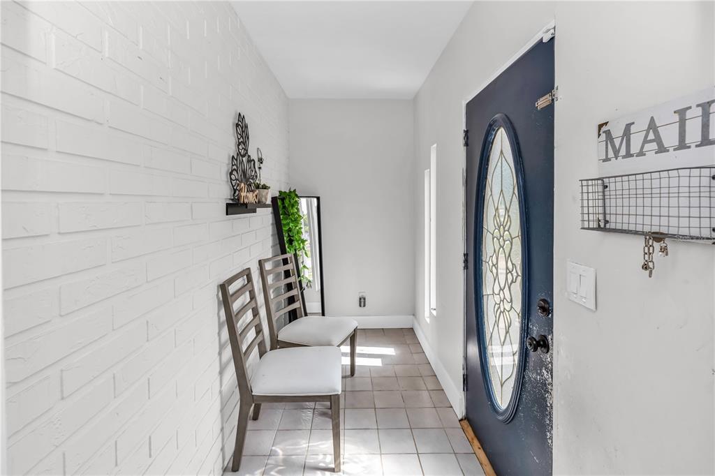 An entryway features a white brick wall, tiled floor, two chairs, and a blue door — 1020 COBBLESTONE AVENUE, DELTONA, FL