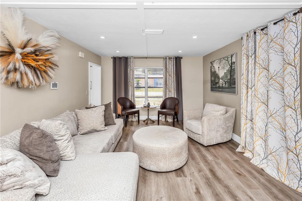 A living room features a sectional sofa, two armchairs, a round ottoman, and wood flooring — 1020 COBBLESTONE AVENUE, DELTONA, FL