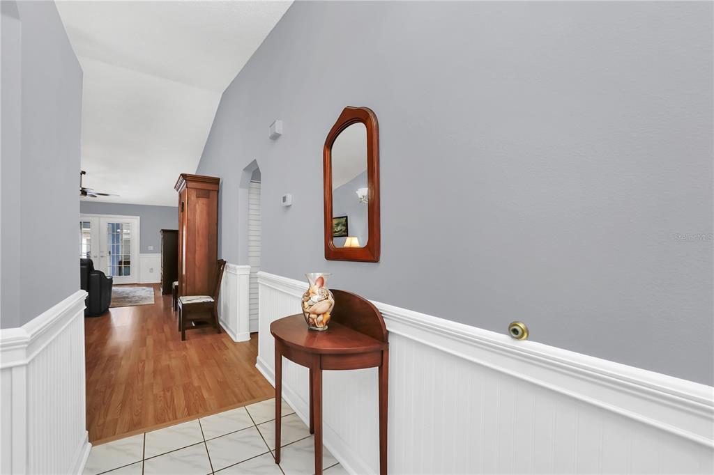 A hallway with white wainscoting, a wooden console table, a mirror, and wood flooring — 909 ILLINOIS AVENUE, ST CLOUD, FL