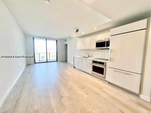 A modern kitchen with light wood cabinetry and stainless steel appliances opens to a living area — 45 SW 9th St # 3009, Miami FL 33130, MIAMI, FL
