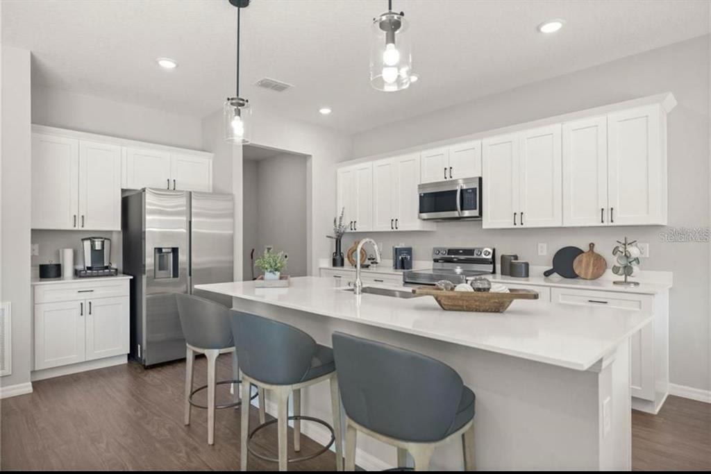 A modern kitchen features white cabinets, stainless steel appliances, a large island, and gray stools — 5191 SW 159TH ST, OCALA, FL