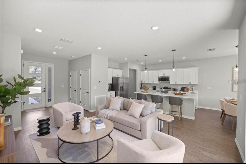 An open-concept living room and kitchen featuring light wood floors, white cabinets, and neutral furniture — 5191 SW 159TH ST, OCALA, FL