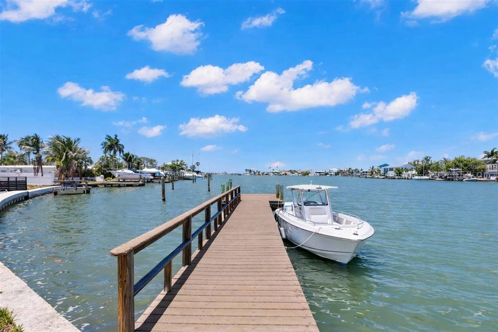 A wooden dock extends into a canal with a white boat moored alongside — 708 SUNSET COVE, MADEIRA BEACH, FL