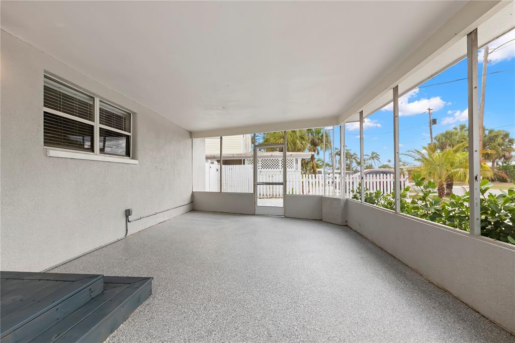 A covered screened-in porch with a speckled concrete floor and a small wooden step — 708 SUNSET COVE, MADEIRA BEACH, FL