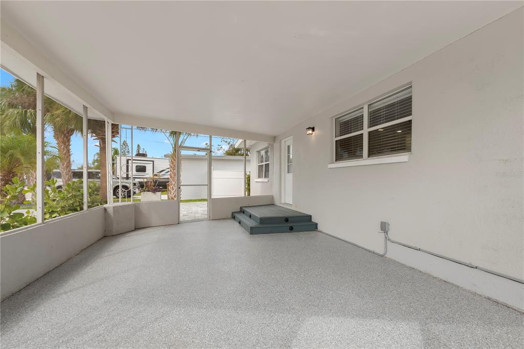 A covered screened-in patio features a gray speckled floor, blue steps, and white walls — 708 SUNSET COVE, MADEIRA BEACH, FL