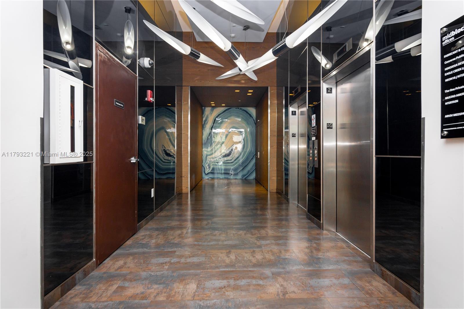 A modern building lobby features metallic elevator doors, mirrored walls, and a decorative blue mural — 3250 NE 1st Ave # 608, Miami FL 33137, MIAMI, FL