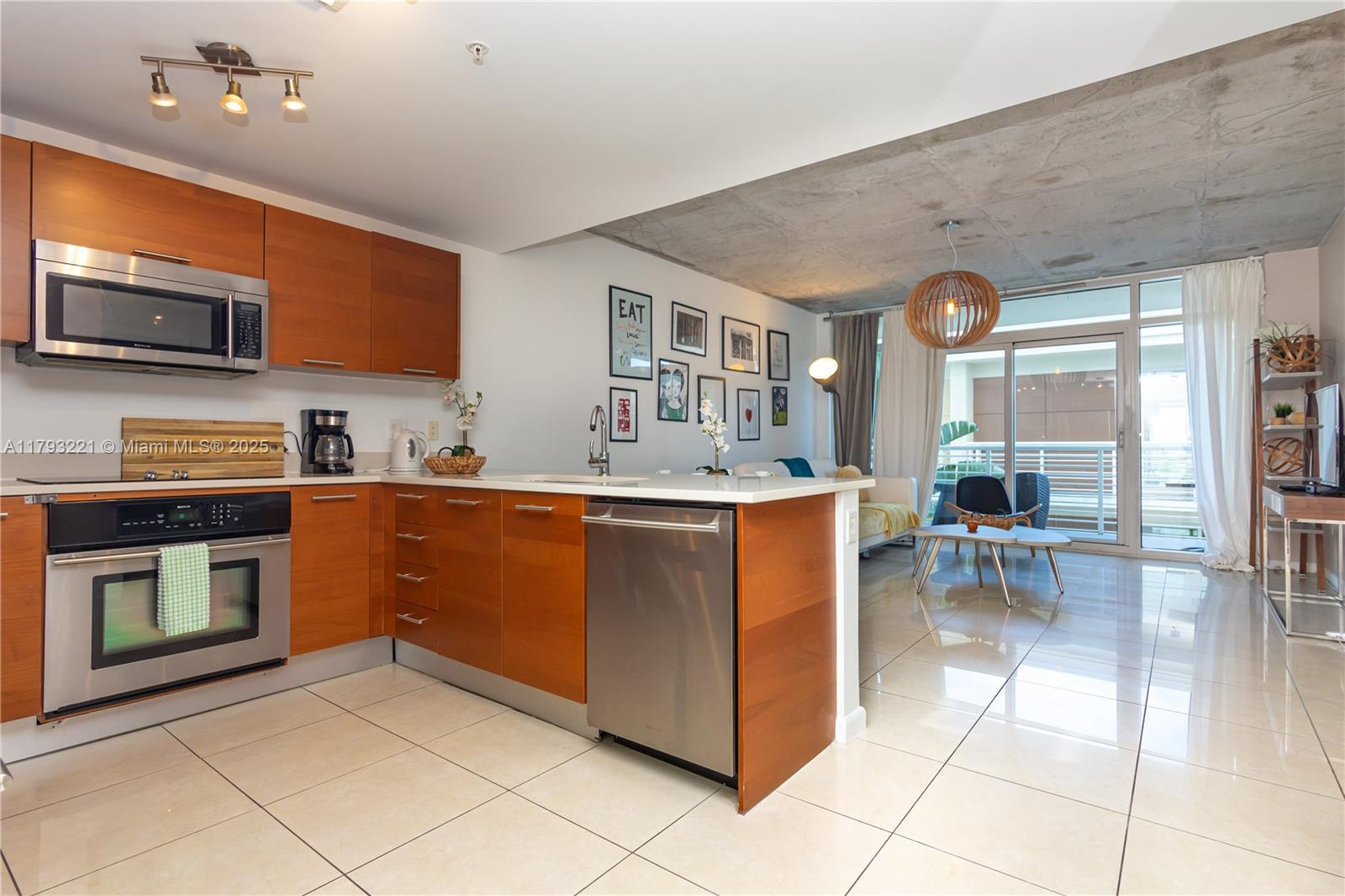 A modern kitchen with wood cabinets and stainless steel appliances opens into a living area — 3250 NE 1st Ave # 608, Miami FL 33137, MIAMI, FL