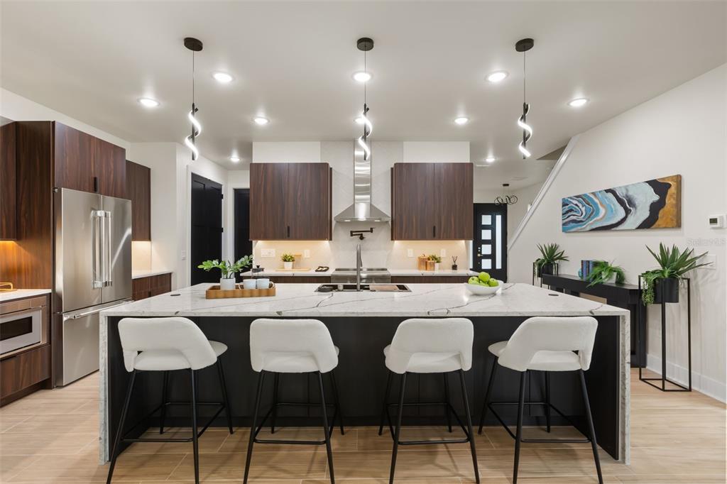 A modern kitchen features a large white marble island, dark wood cabinetry, and four stools — 1910 CLOVERLAWN AVENUE, ORLANDO, FL