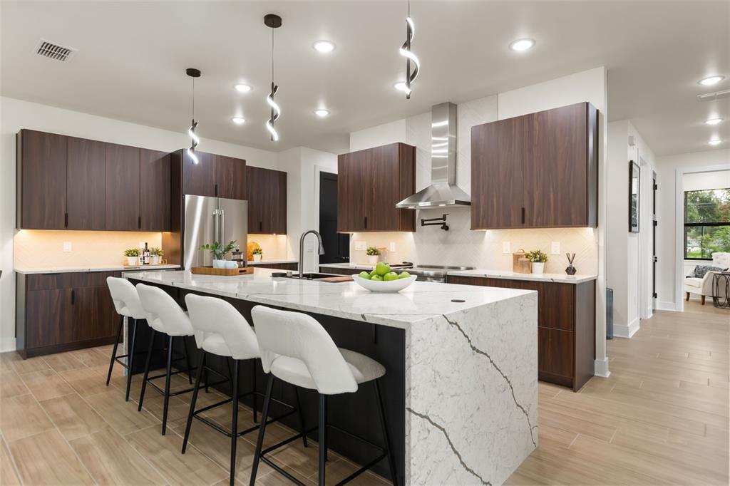A modern kitchen features dark wood cabinetry, a large marble island, and white bar stools — 1910 CLOVERLAWN AVENUE, ORLANDO, FL