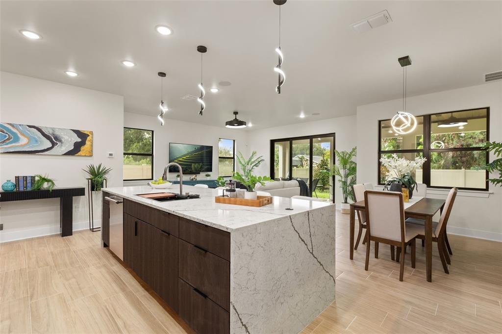 A modern kitchen features a large marble-topped island, dark wood cabinetry, and an adjacent dining area — 1910 CLOVERLAWN AVENUE, ORLANDO, FL