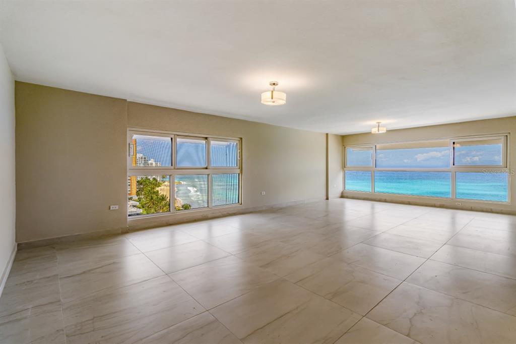 An empty room with large windows overlooking the ocean and light-colored tile flooring — 1507 ASHFORD AVE. UNIT 1002, SAN JUAN, PR
