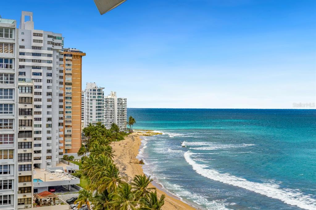 An aerial view shows a tall apartment building next to a sandy beach and ocean — 1507 ASHFORD AVE. UNIT 1002, SAN JUAN, PR