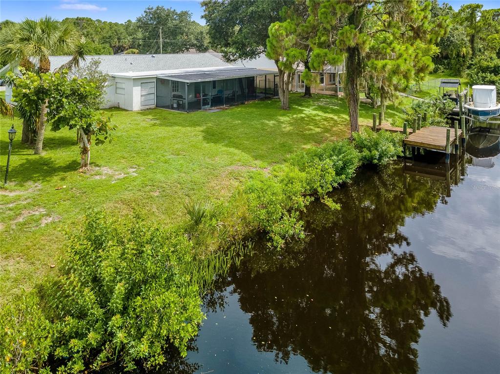 A backyard with a lawn, a screened-in patio, and a wooden dock on a canal — 297 CHESHIRE STREET, PORT CHARLOTTE, FL