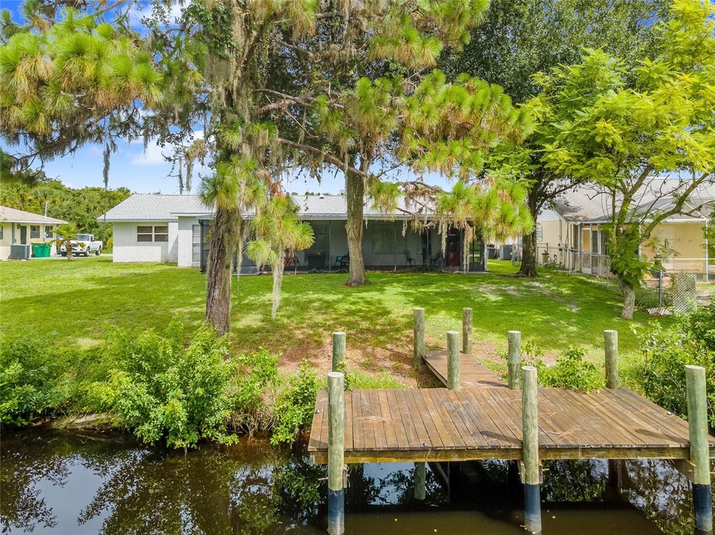 A backyard with a wooden dock extending into a canal behind a single-story house — 297 CHESHIRE STREET, PORT CHARLOTTE, FL