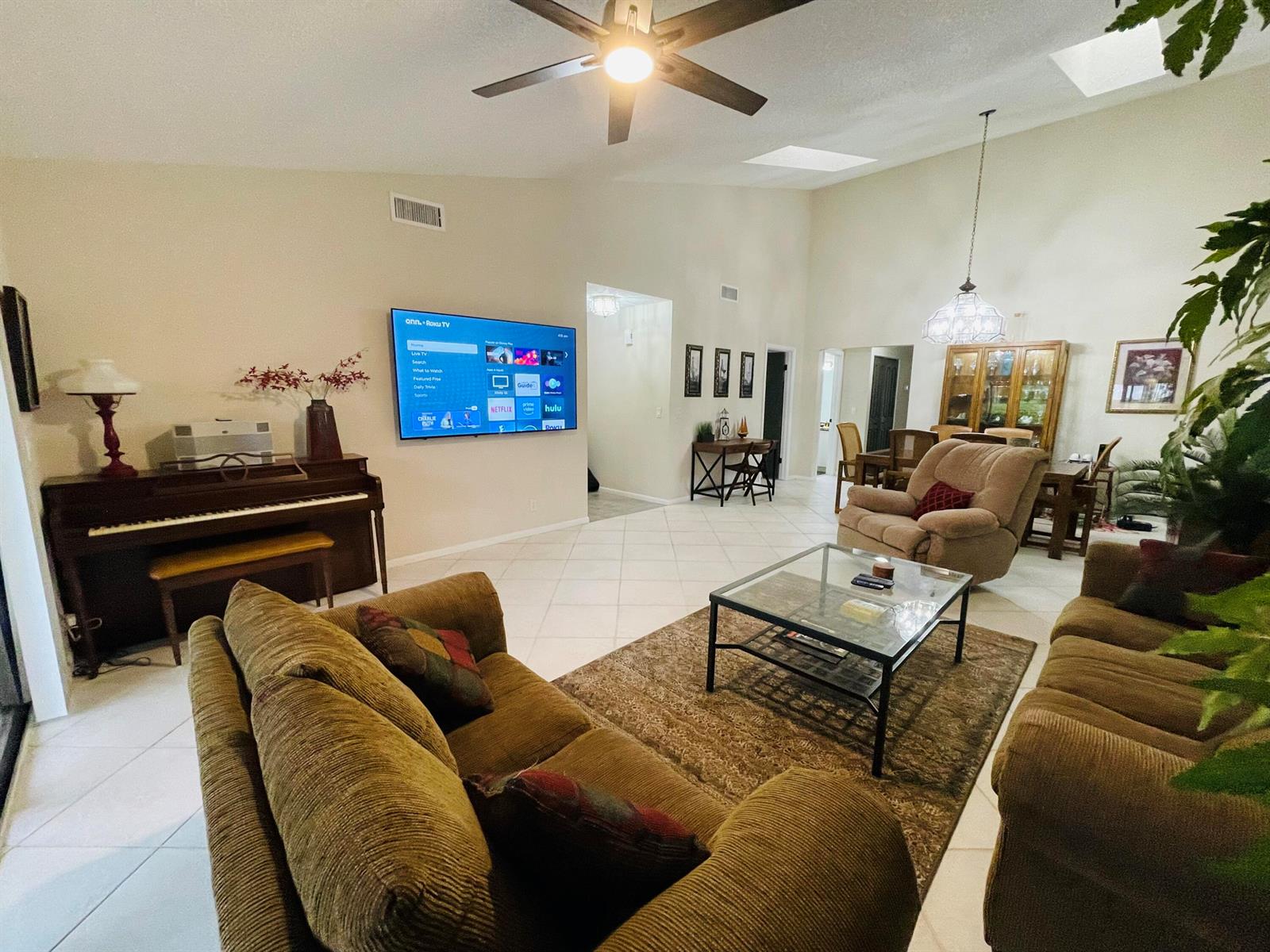 A spacious living room features a piano, a wall-mounted television, and tile flooring — 354 SW 28th Avenue, Delray Beach FL 33445, DELRAY BEACH, FL